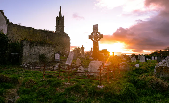 Church ruins and a stone cross at sunset; an illustrative scene for Irish family history.